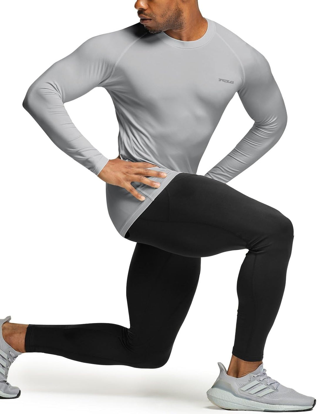 Mann in grauem Kompressionsshirt und schwarzen Leggings beim Ausfallschritt, Sportbekleidung.