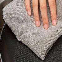 Hand wischt mit grauem Mikrofasertuch über Pfanne, Reinigung, Küchenzubehör, Haushaltspflege.