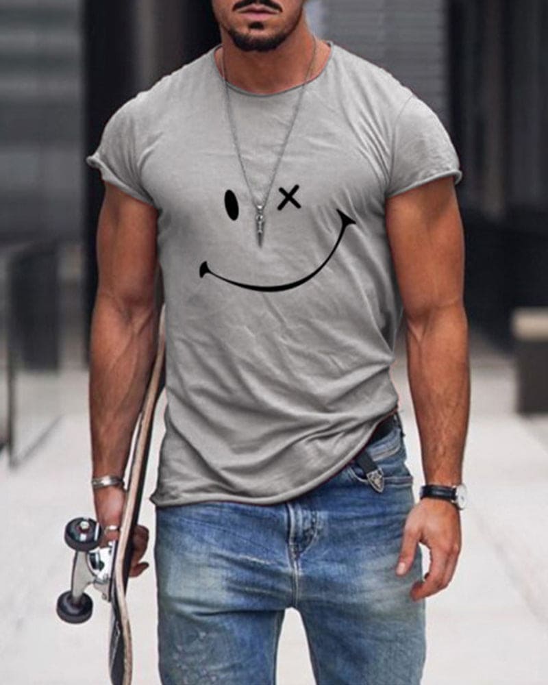 Mann in grauem T-Shirt mit Smiley-Design, Jeans, Skateboard, urbaner Hintergrund.