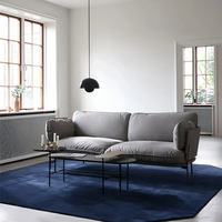 Graues Sofa im modernen Wohnzimmer, blauer Teppich, schwarze Hängelampe, große Fenster.