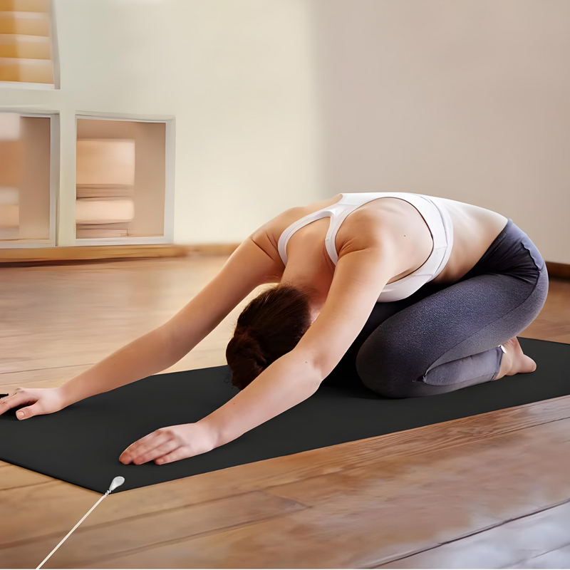 Frau in Yoga-Pose auf schwarzer Yogamatte in hellem Raum, Sportbekleidung, Entspannung.