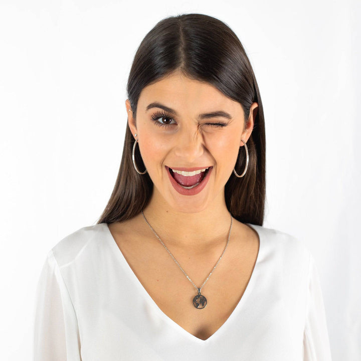 Frau mit großen silbernen Creolen und Halskette, lächelnd, weißes Oberteil.