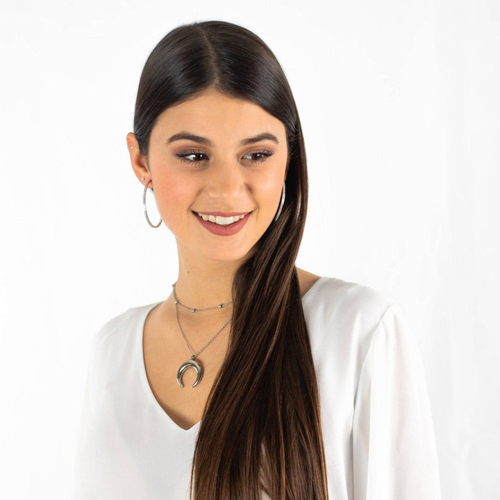 Frau mit großen silbernen Creolen und Hufeisenkette, eleganter Schmuck, weißes Oberteil.