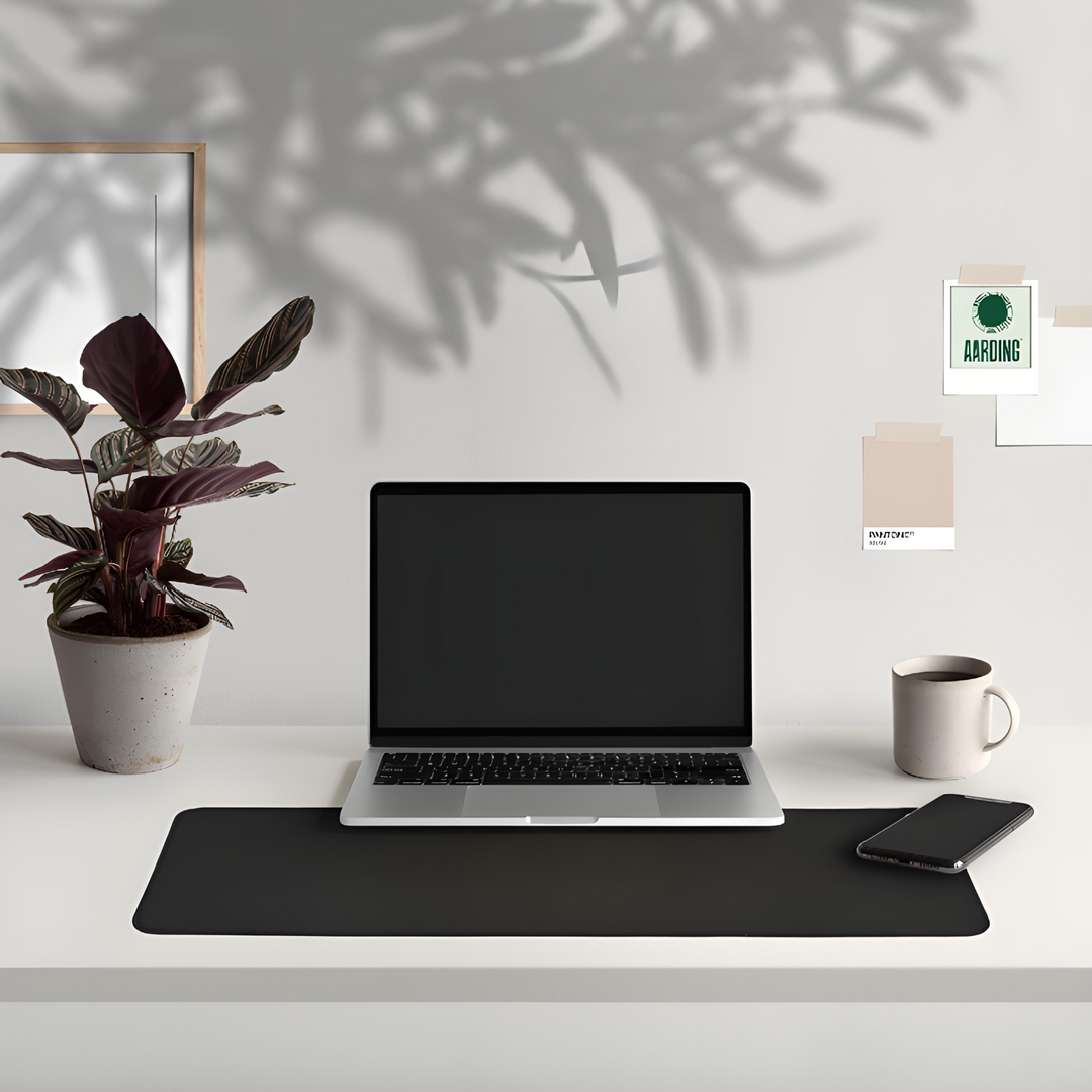 Laptop auf Schreibtisch mit schwarzer Matte, Pflanze, Tasse und Smartphone, modernes Büro-Setup.