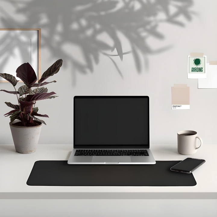 Laptop auf Schreibtisch mit schwarzer Matte, Pflanze, Tasse und Smartphone, modernes Büro-Setup.