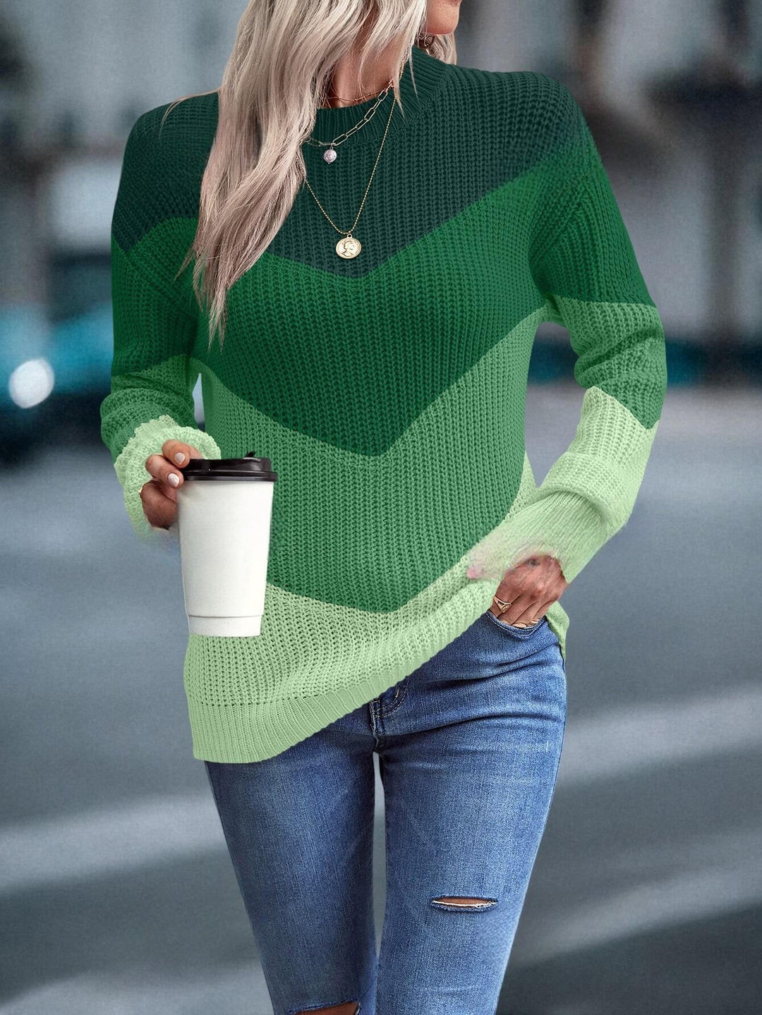 Frau in grünem Strickpullover mit Kaffeebecher, Jeans, Straße, modisch, lässig, Herbstmode.