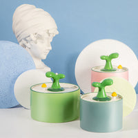 Deko-Objekte mit grünen Knöpfen, pastellfarbenen Dosen, Büste im Hintergrund, modernes Design.