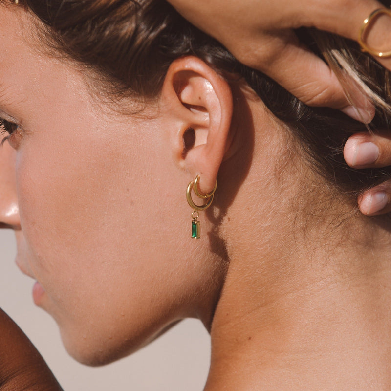 Frau mit goldenen Ohrringen und grünem Anhänger, Sommermode, Schmucktrends 2023.