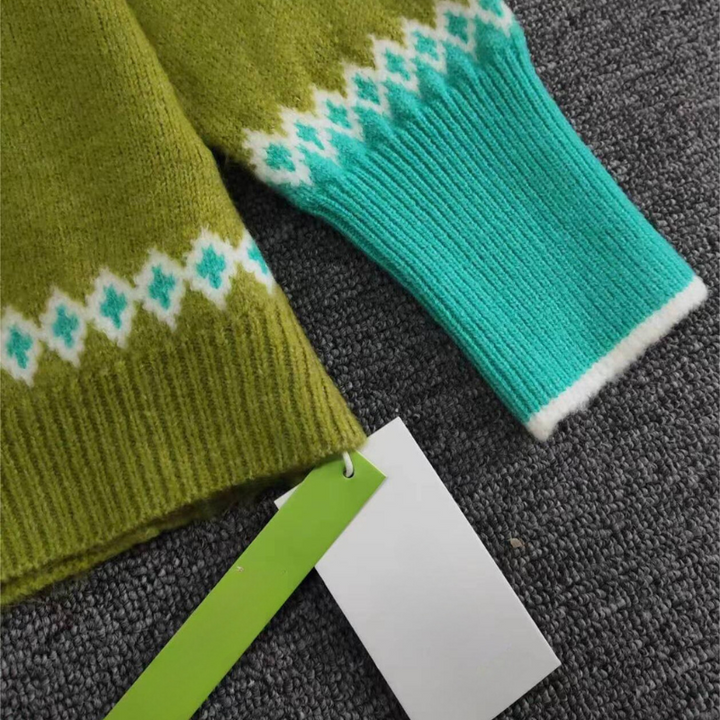 Grüner und blauer Strickpullover mit Zickzackmuster, Etikett, auf grauem Hintergrund.
