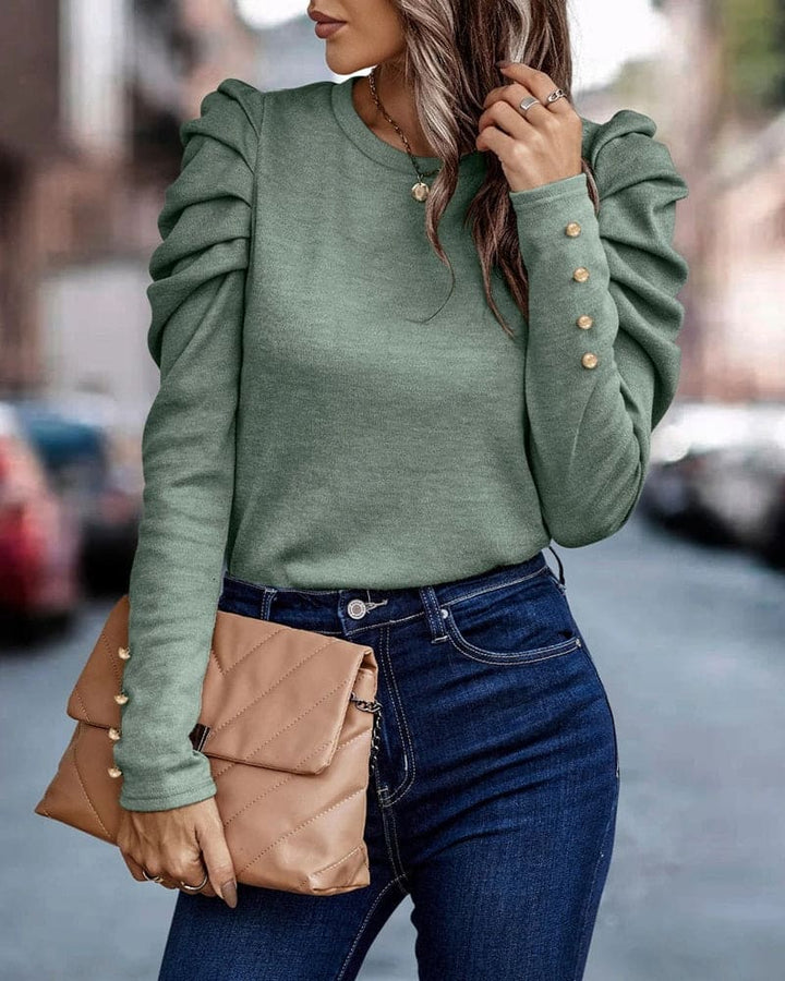 Frau in grünem Rüschenpullover, blaue Jeans, beige Clutch, Stadtstraße Hintergrund.