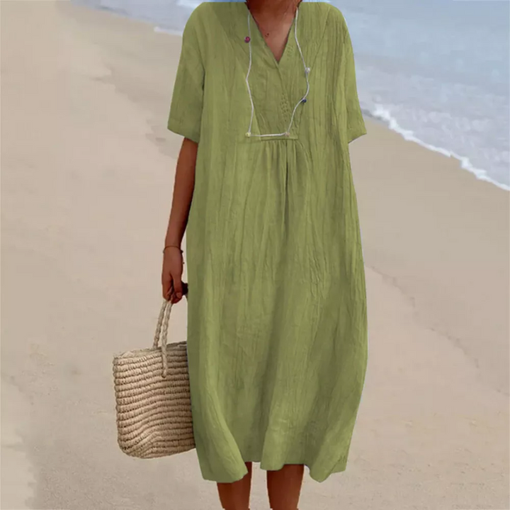 Frau in grünem Leinenkleid am Strand mit Strohtasche, Sommermode, lässiger Stil.