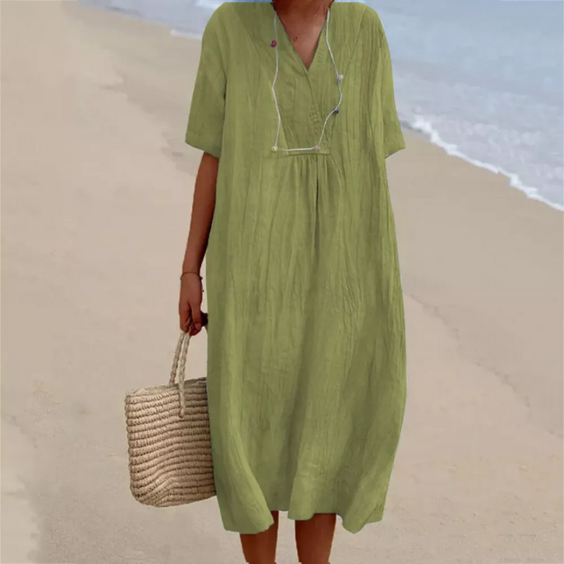 Frau in grünem Leinenkleid am Strand mit Strohtasche, Sommermode, lässiger Stil.