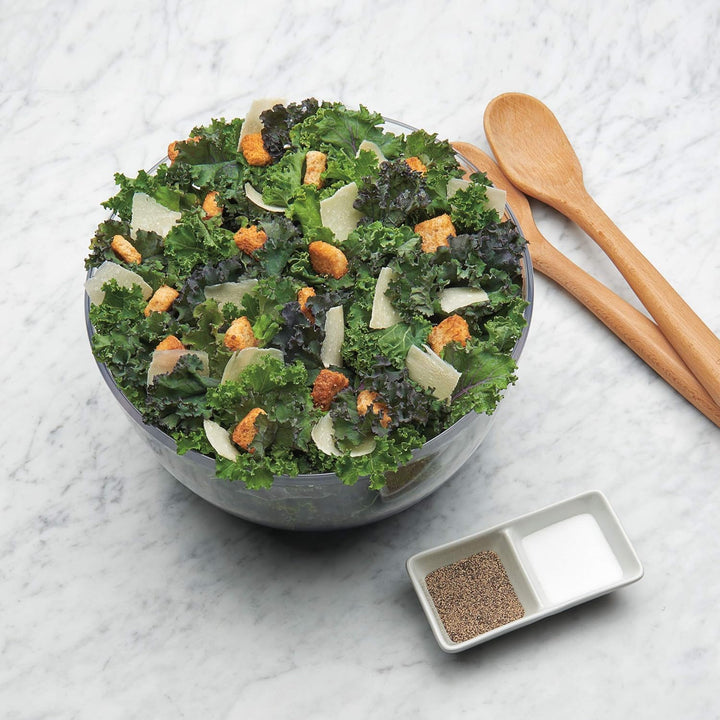 Grüner Salat mit Croutons und Parmesan in Glasschüssel auf Marmortisch, Holzlöffel daneben.