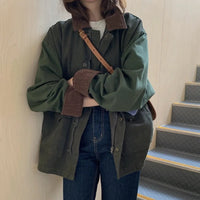Frau in grüner Oversize-Jacke mit braunem Kragen, Jeans und Umhängetasche an Treppe.