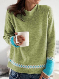 Frau in grünem Strickpullover mit blauem Muster hält weiße Tasse, lässige Mode.