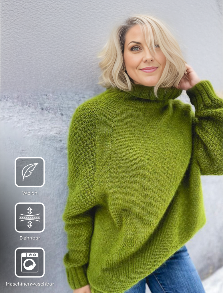 Frau in grünem Strickpullover, weich, dehnbar, maschinenwaschbar, vor grauer Wand.