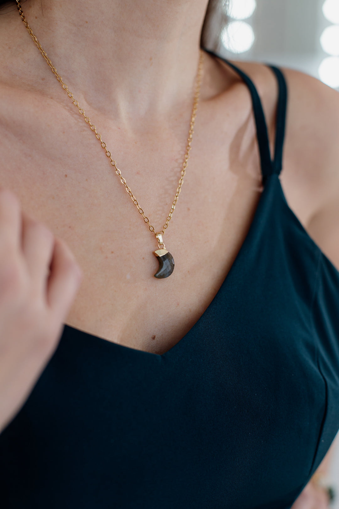 Frau mit goldener Halskette und schwarzem Anhänger, elegantes Schmuckstück, Nahaufnahme.