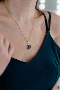 Frau mit goldener Halskette und schwarzem Anhänger, elegantes Schmuckstück, Nahaufnahme.