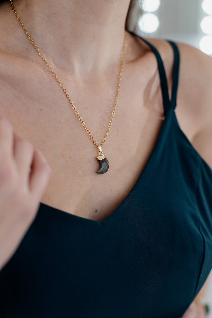 Frau mit goldener Halskette und schwarzem Anhänger, elegantes Schmuckstück, Nahaufnahme.