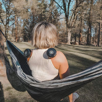 Frau in Hängematte mit Massagegeräten auf Schultern im Wald, Entspannung, Outdoor, Freizeit.