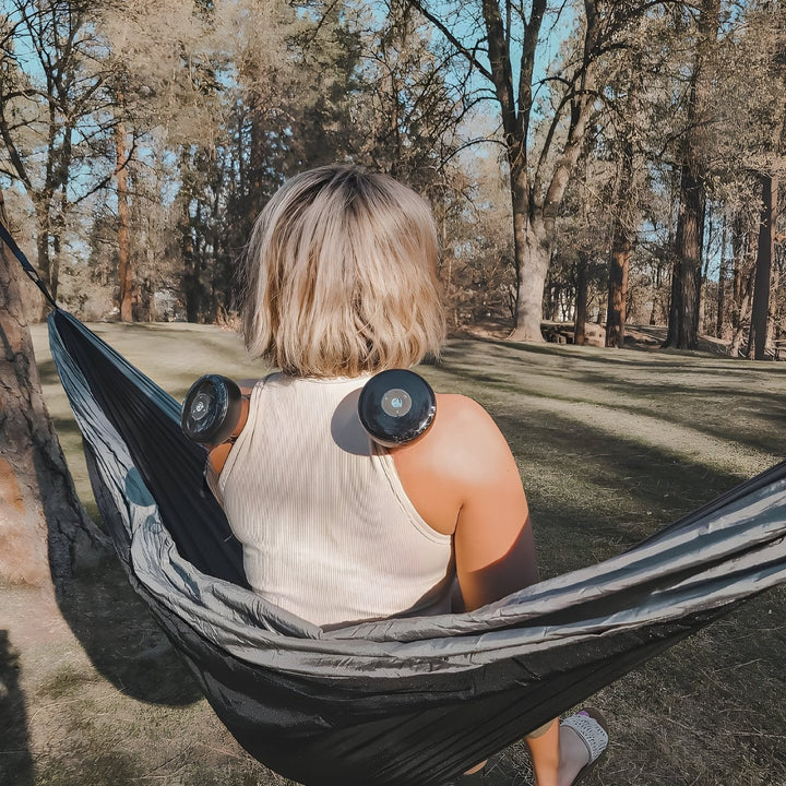 Frau in Hängematte mit Massagegeräten auf Schultern im Wald, Entspannung, Outdoor, Freizeit.