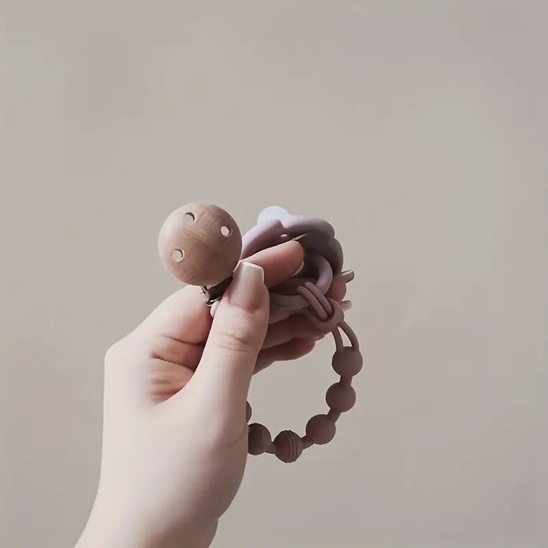 Hand hält Holz-Schnullerkette mit Silikonperlen, beige und rosa, Babyzubehör.