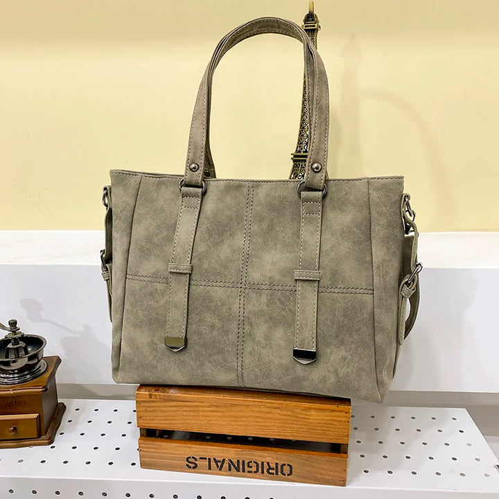 Graue Damenhandtasche aus Leder mit Trageriemen auf Holzkiste im modernen Design.