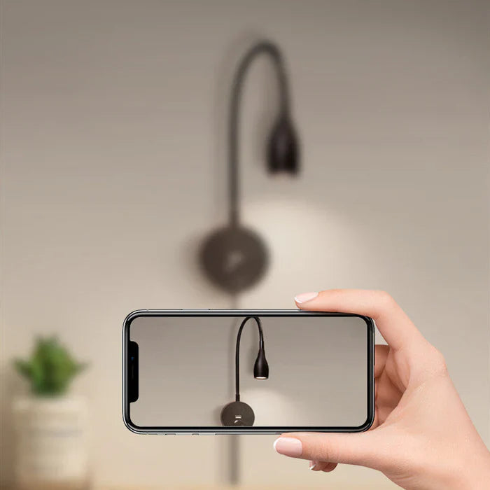 Hand hält Smartphone, fokussiert auf moderne schwarze Wandlampe, unscharfer Hintergrund.