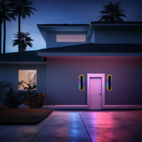 Moderne Hausfassade bei Nacht mit bunter LED-Beleuchtung, Palmen im Hintergrund.