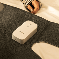 Graues Massagegerät auf Stoff, tragbar, kabellos, für Nacken- und Schultermassage, moderne Technologie.