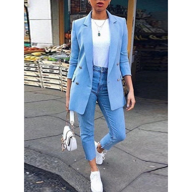 Frau in hellblauem Blazer, weißem Shirt, Jeans und Sneakers auf der Straße.