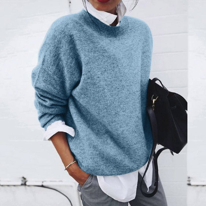 Frau in blauem Strickpullover, weißem Hemd, grauer Hose, schwarze Tasche, lässiger Stil.