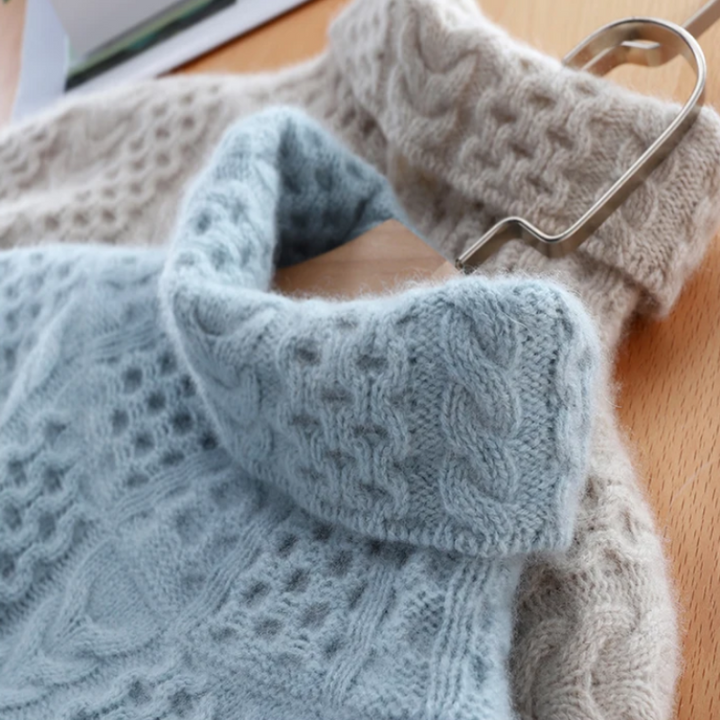 Blaue und beige Strickpullover aus Wolle mit Zopfmuster auf Holztisch.