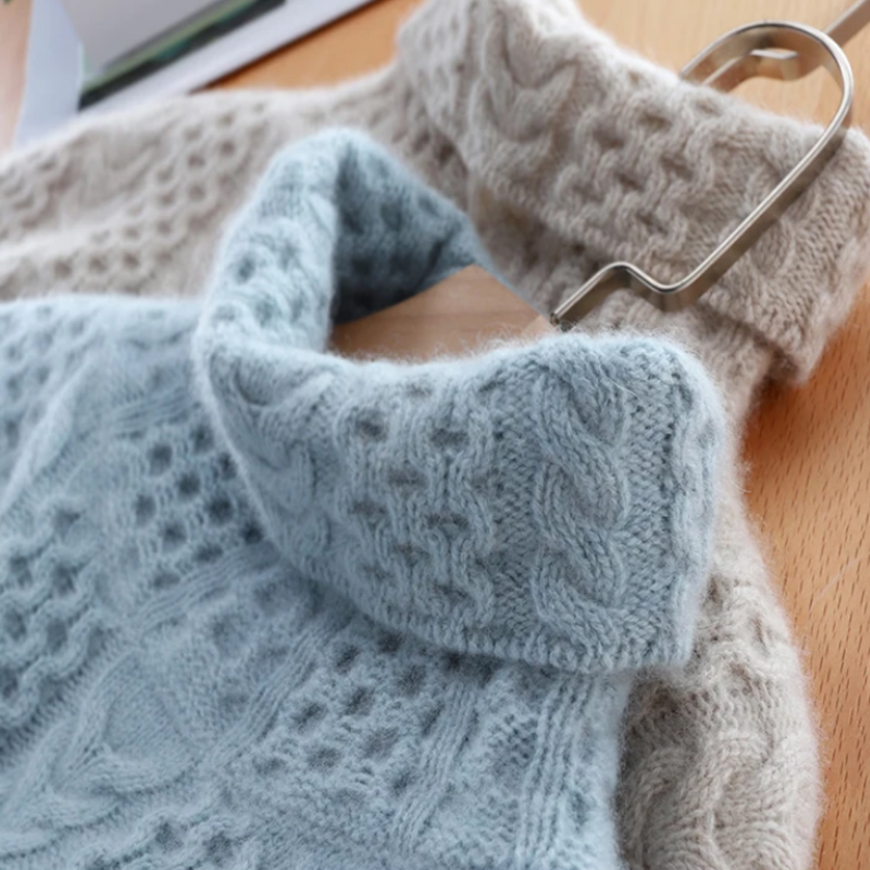 Blaue und beige Strickpullover aus Wolle mit Zopfmuster auf Holztisch.