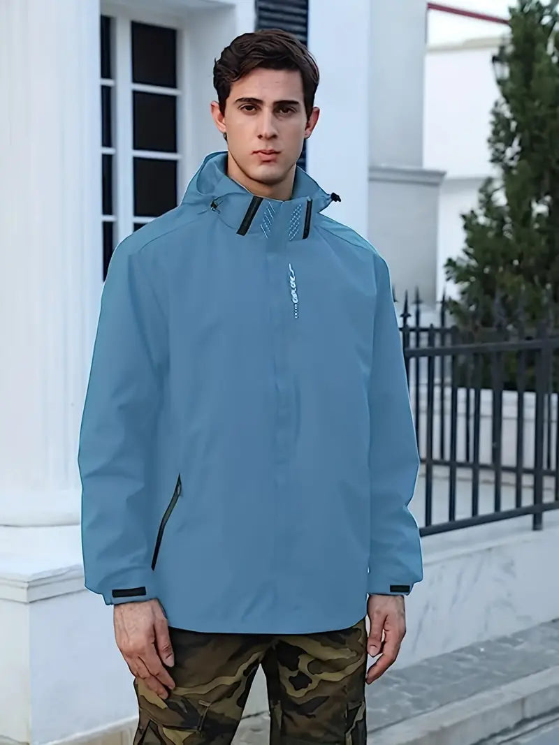 Mann in blauer Outdoor-Jacke, Kapuze, Reißverschluss, vor Gebäude, modisch, funktional.