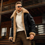Mann in schwarzer, gefütterter Winterjacke mit Fellkragen, Sonnenbrille, weißem Rollkragenpullover.