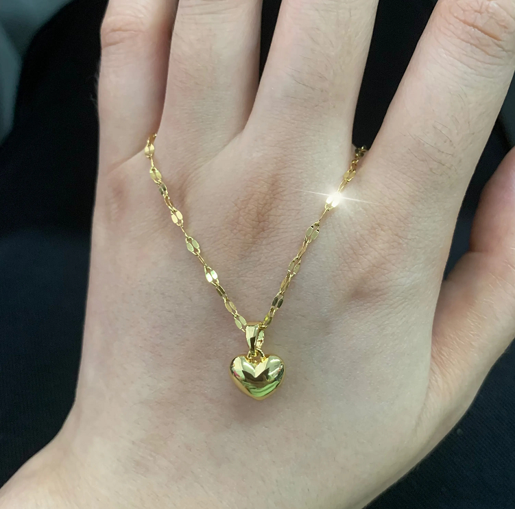 Goldene Herz-Halskette auf Hand, glänzend, elegantes Schmuckstück, modisches Accessoire.