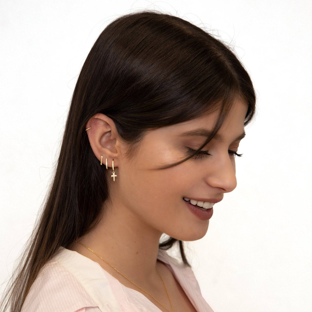 Frau mit goldenen Kreuz-Ohrringen, lächelnd, braunes Haar, weißer Hintergrund.