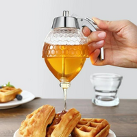 Hand hält Honigspender aus Glas über Waffeln, Honig fließt heraus, Frühstück, Küche.