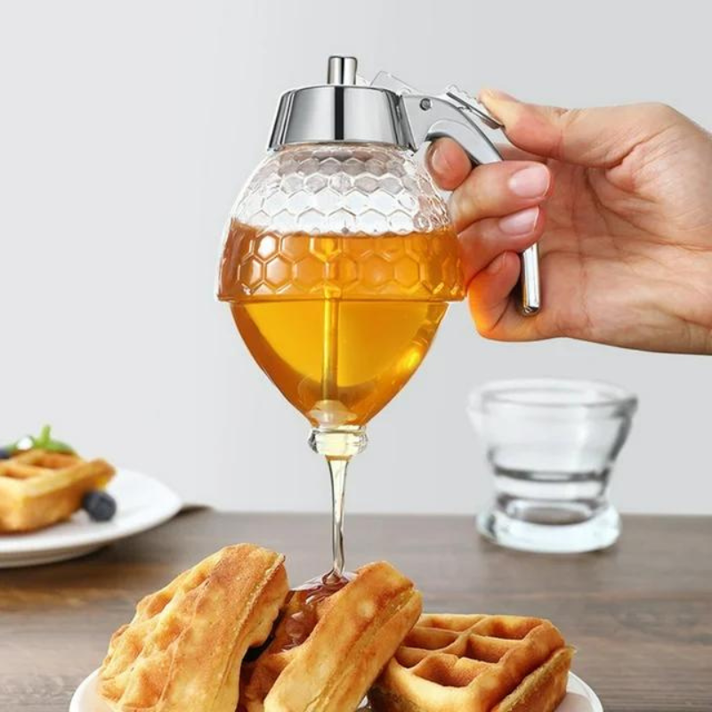 Hand hält Honigspender aus Glas über Waffeln, Honig fließt heraus, Frühstück, Küche.
