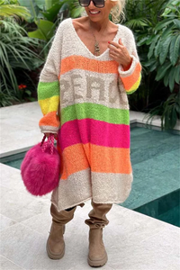 Frau in buntem Strickcardigan mit Regenbogenstreifen, rosa Tasche, braune Stiefel, draußen.