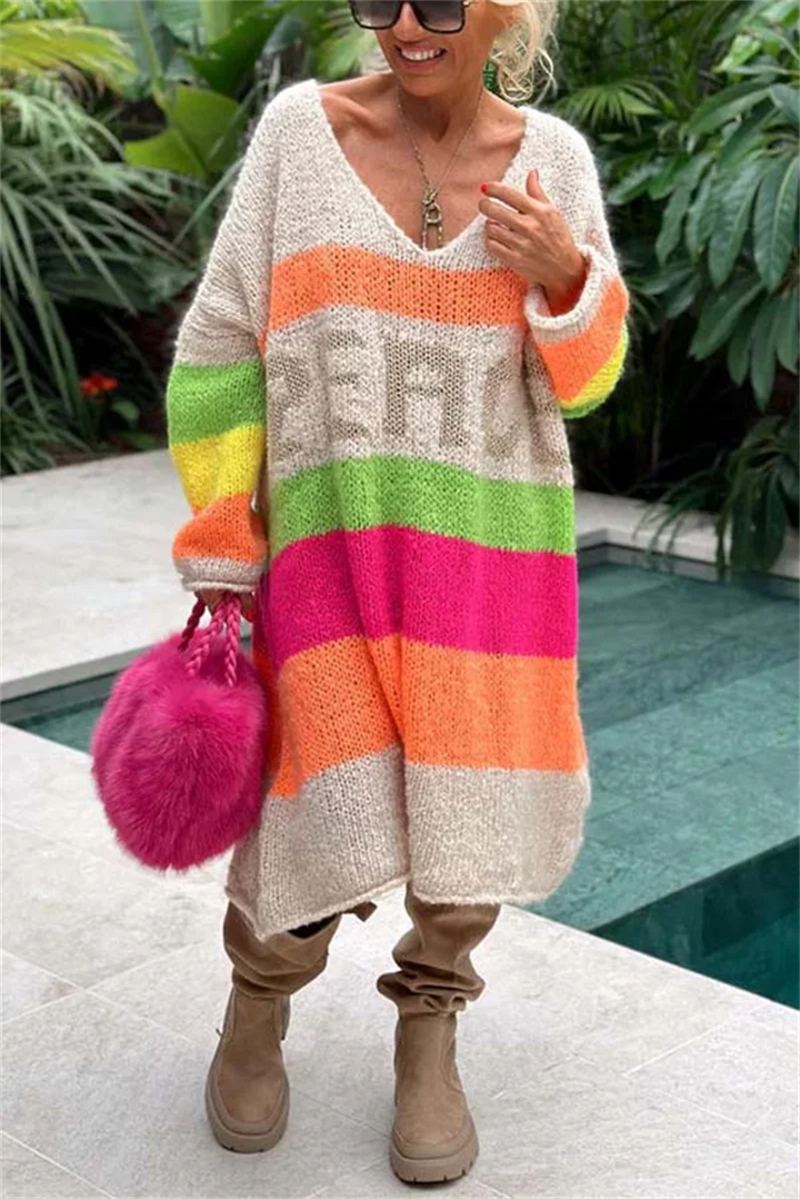 Frau in buntem Strickcardigan mit Regenbogenstreifen, rosa Tasche, braune Stiefel, draußen.