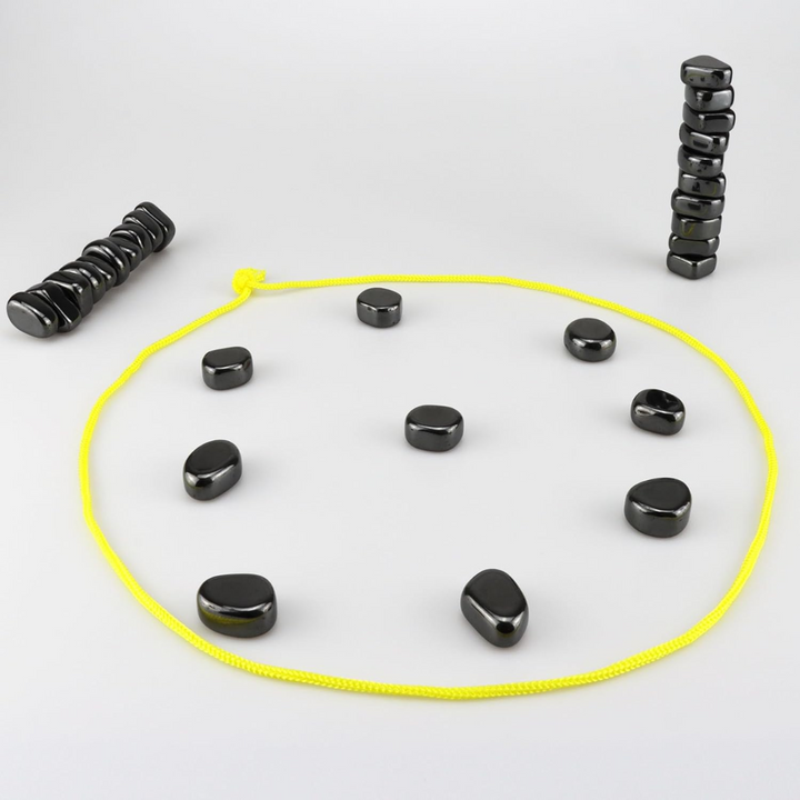 Schwarze Steine im Kreis mit gelbem Seil, auf grauem Hintergrund, Meditations-Set.