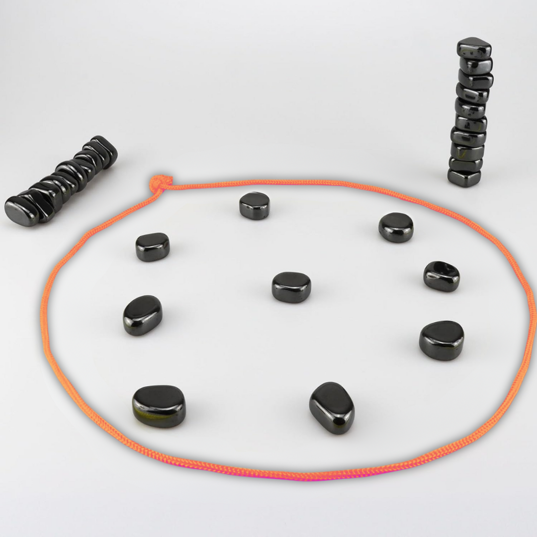 Schwarze Magnetsteine auf weißem Hintergrund, orangefarbene Schnur, Stapel und Kreisformation.