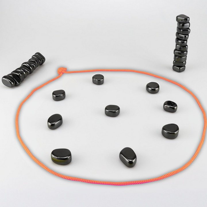 Schwarze Magnetsteine auf weißem Hintergrund, orangefarbene Schnur, Stapel und Kreisformation.