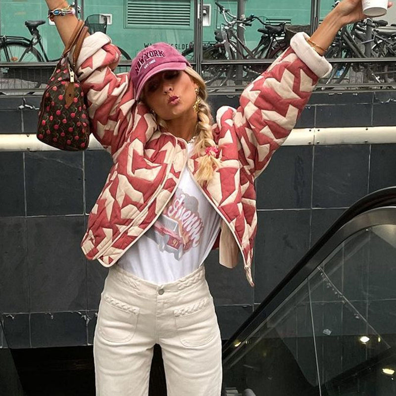 Frau in roter geometrischer Jacke, weißem T-Shirt, rosa Mütze, hält Tasche und Kaffeebecher.