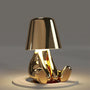 Goldene Tischlampe in Form einer sitzenden Figur, modernes Design, warmes Licht.