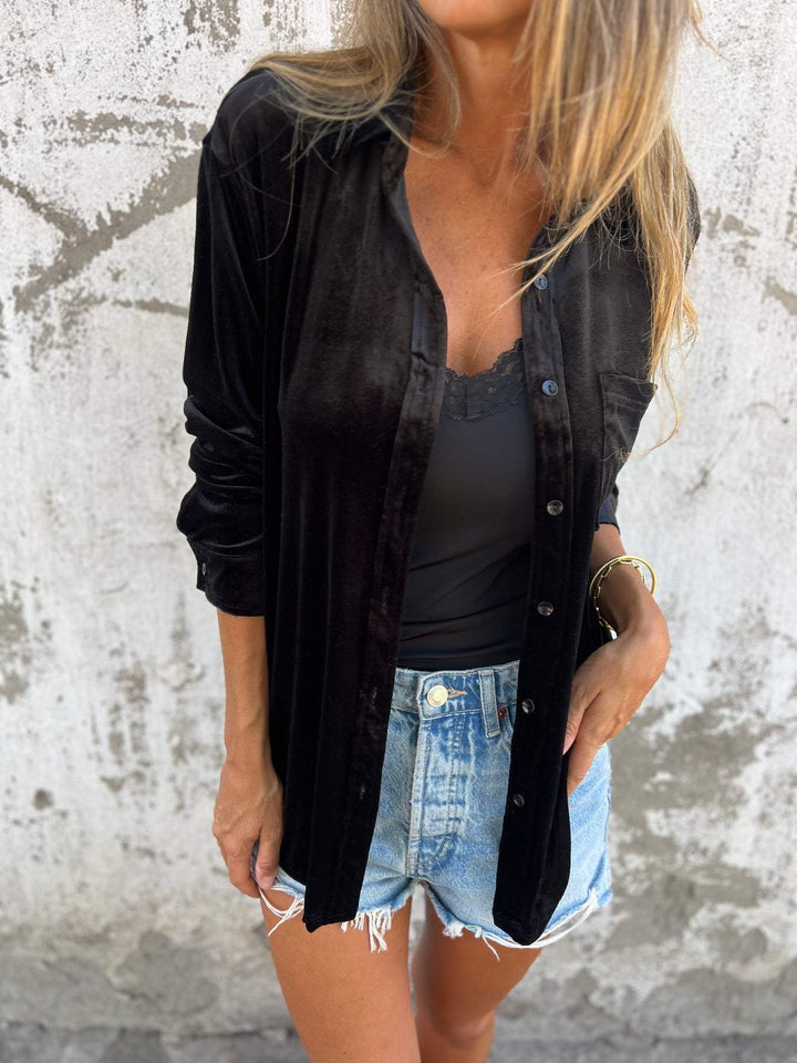 Frau in schwarzer Bluse und Jeansshorts vor Betonwand, lässige Mode, Streetstyle-Look.