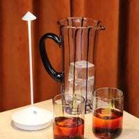 Karaffe mit Eiswürfeln, zwei Gläser mit Getränk, moderne weiße Tischlampe, stilvolles Design.