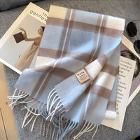 Kariertes Kaschmirschal in Weiß und Beige auf grauem Sofa, modisches Accessoire.